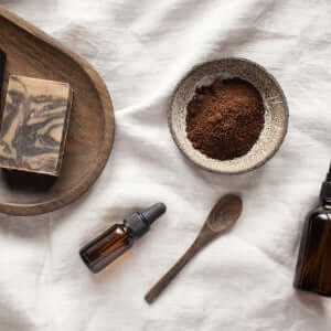 Coffee Face Scrub ingredients, including coffee grounds, essential oils, and soap on a textured surface.
