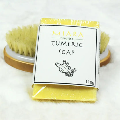 Miara Essence Turmeric Soap packaging next to a natural brush for gentle cleansing and skin nourishment.